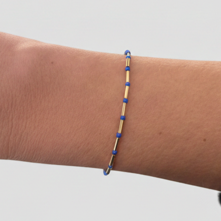 Person wearing a thin blue and gold bracelet on a white background